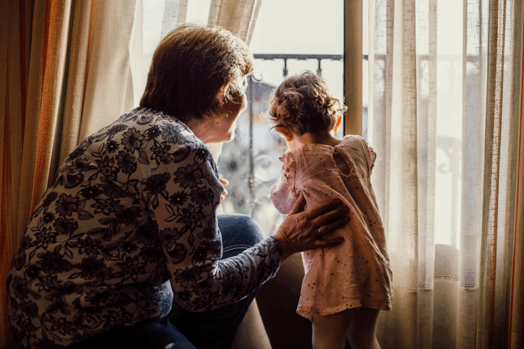 a grandma holding her granddaughter by the window, looking outside