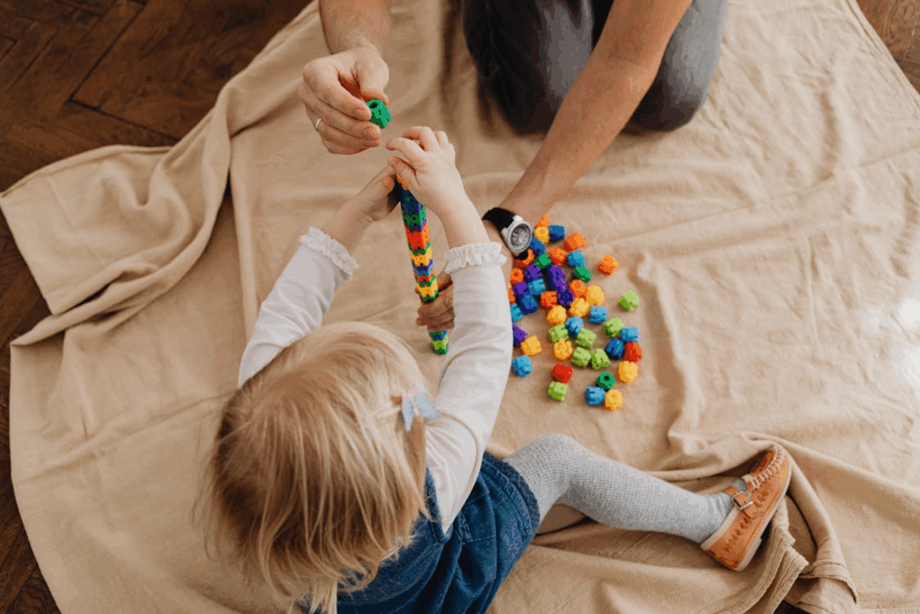 top-view of a kid sitting with their parent on a cloth, playing with blocks