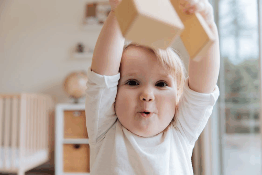 a baby in a onesie holding wooden blocks