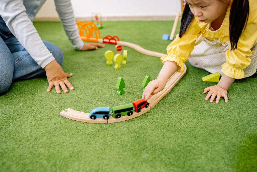 Child in a yellow dress playing with wooden toy cars on a green carpet